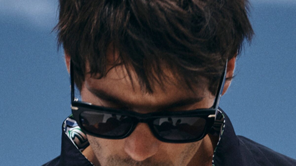 Close-up of a man wearing dark sunglasses outdoors against a blue sky.