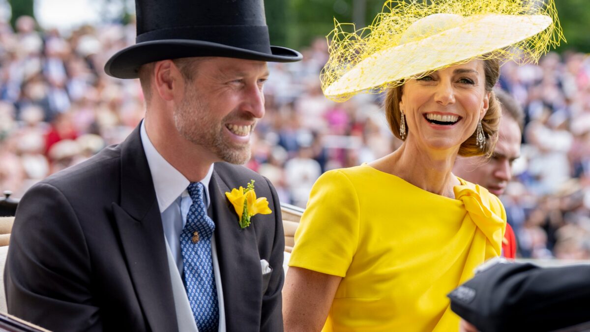 Smiling couple in formal attire on a carriage ride: man in a black tuxedo with a top hat, woman in a bright yellow dress with a matching yellow fascinator.