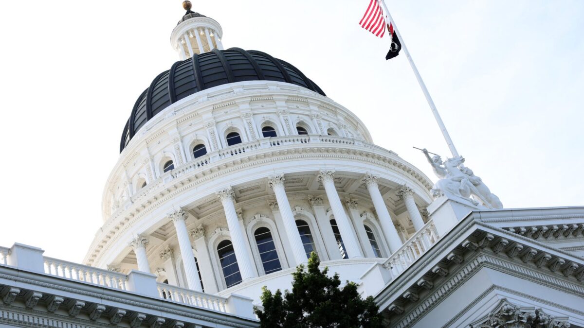White domed government building with a black dome, ornate arches, and an American flag atop the flagpole.