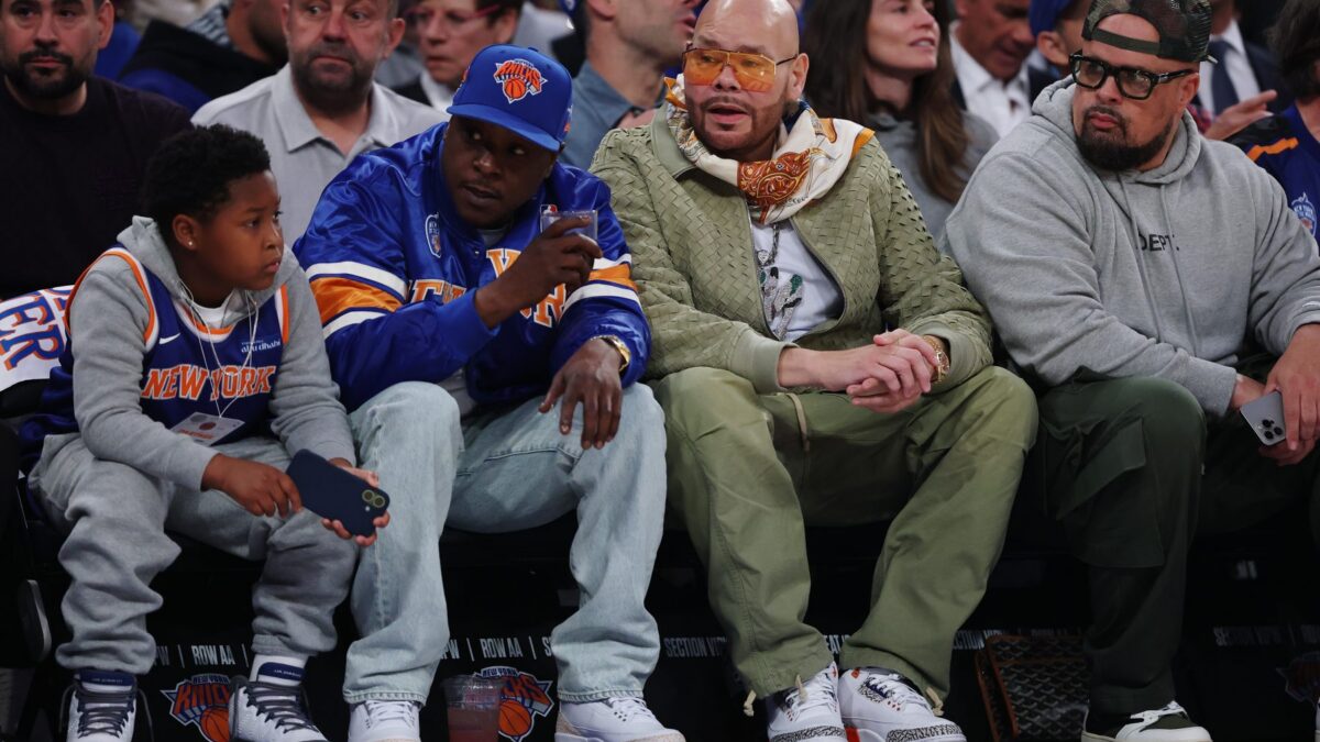 Courtside basketball fans wearing Knicks gear, including a man in orange-tinted glasses and scarf chatting with others.