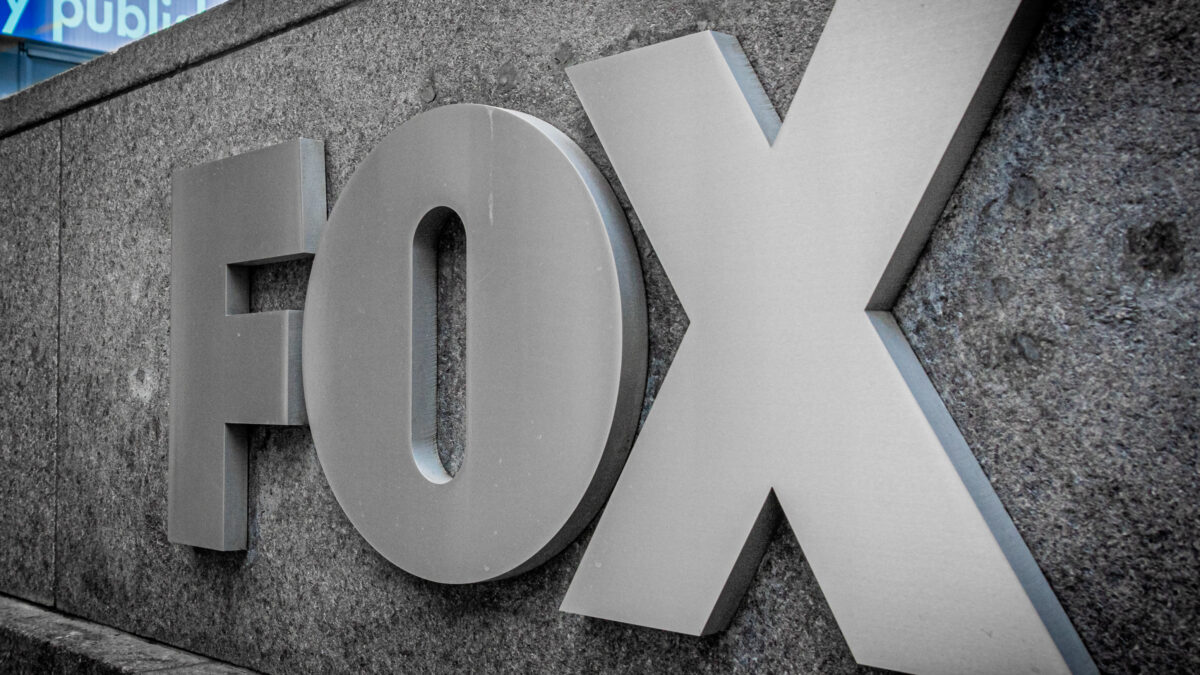 Close-up of large gray metal letters forming 'FOX' mounted on a rough stone wall.