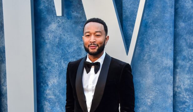Man in a black tuxedo and bow tie posing against a blue textured backdrop at a formal event
