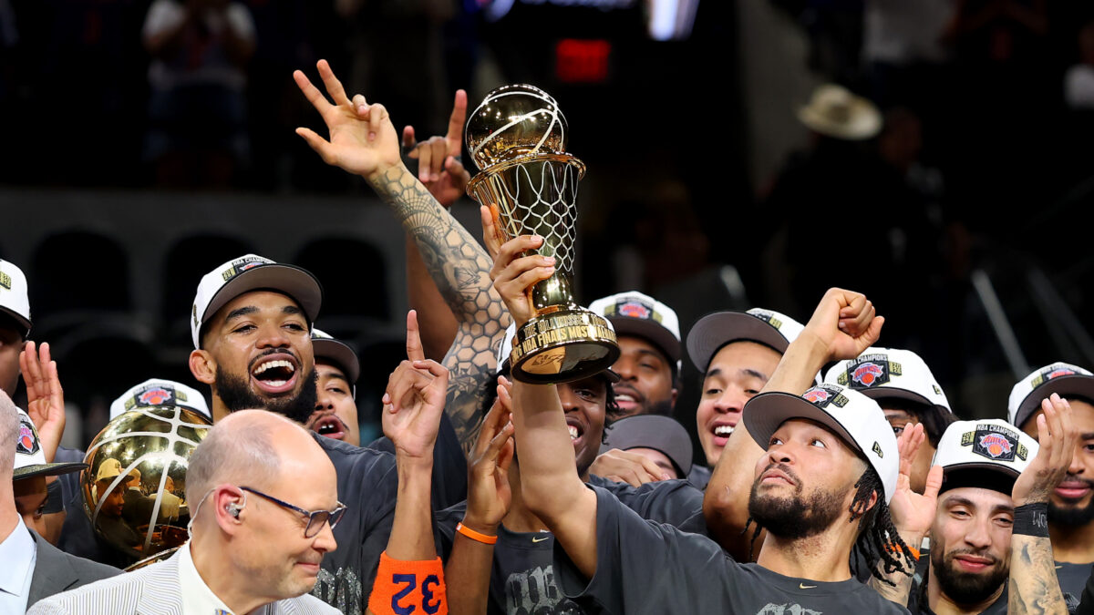 Basketball players and staff celebrate, lifting the NBA Finals trophy as fans cheer nearby.