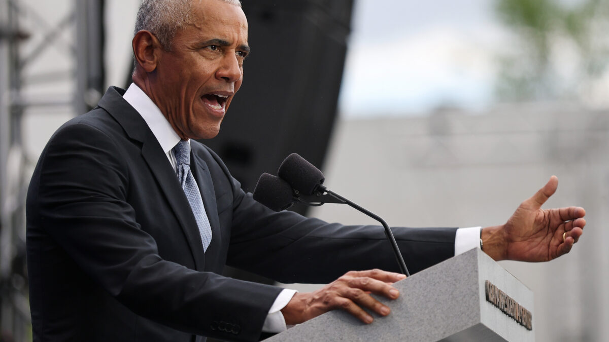 Man in a dark suit delivering a speech at an outdoor podium with two microphones.