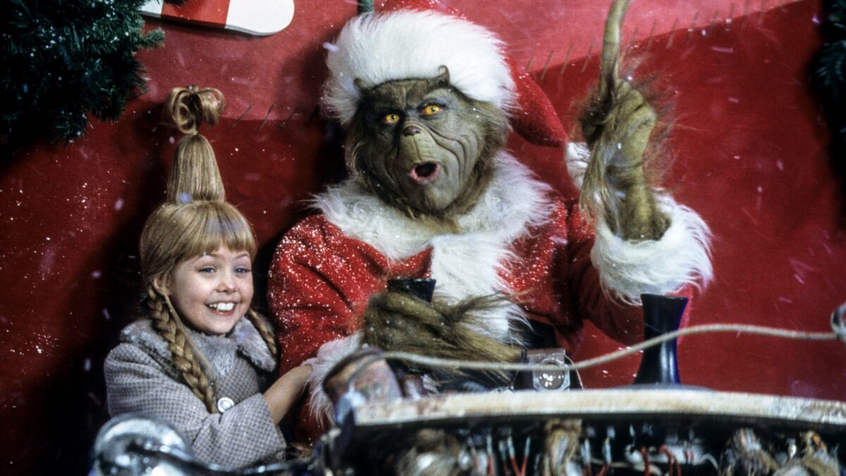 Child smiling with a costumed gorilla in a Santa suit during a holiday display on a festive sleigh.