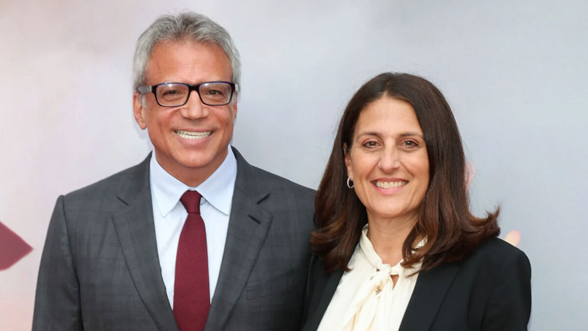 Two smiling professionals posing together in formal attire (man in gray suit and red tie, woman in black blazer and cream blouse).