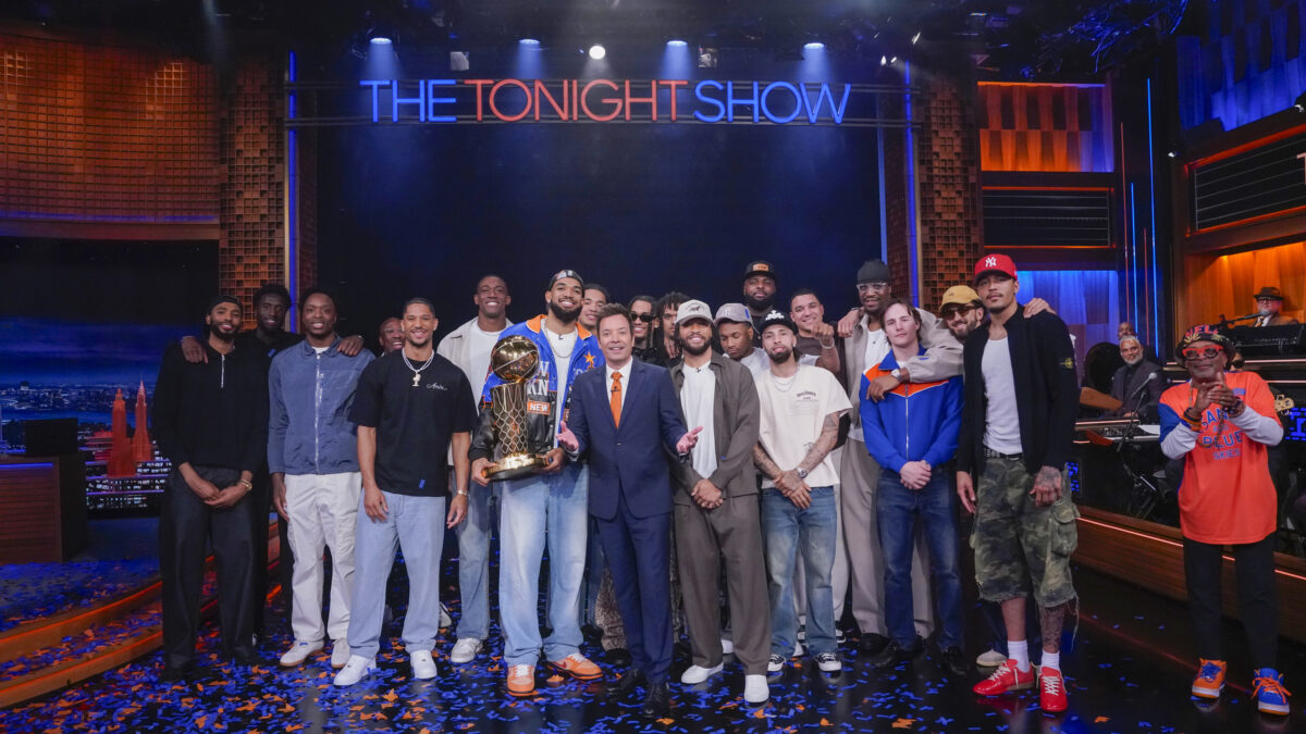 Group of people posing on The Tonight Show stage with a large trophy and blue/orange confetti on the floor.
