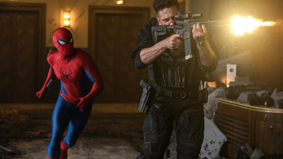 Spider-Man and a heavily armed man fire rifles in a dim, rubble-strewn indoor hallway with muzzle flash.