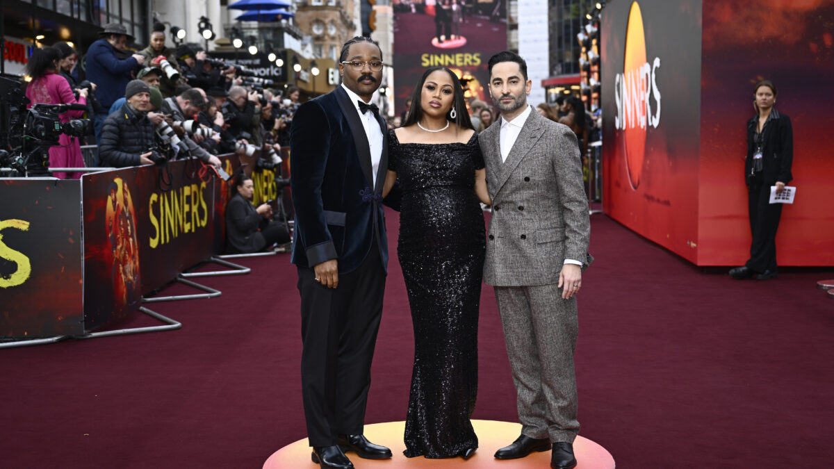 Three celebrities pose on a red carpet premiere, with photographers lining the barriers behind them and a SINNERS backdrop visible behind.