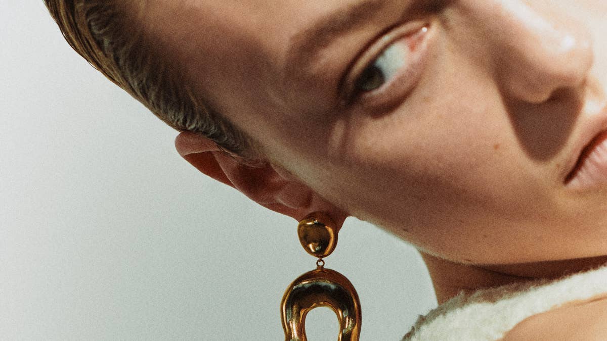 Close-up of a person’s face turned to the side, showcasing a gold statement earring with two linked hoops near the ear.