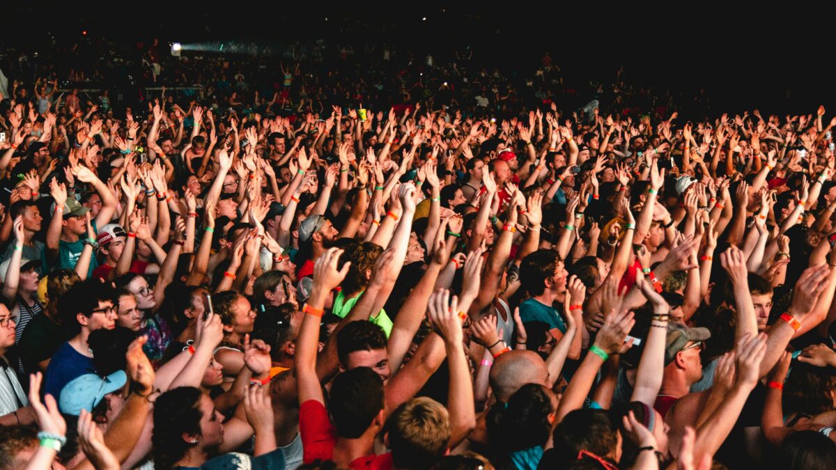 Crowd of concertgoers with raised hands at night, cheering and enjoying a live performance.