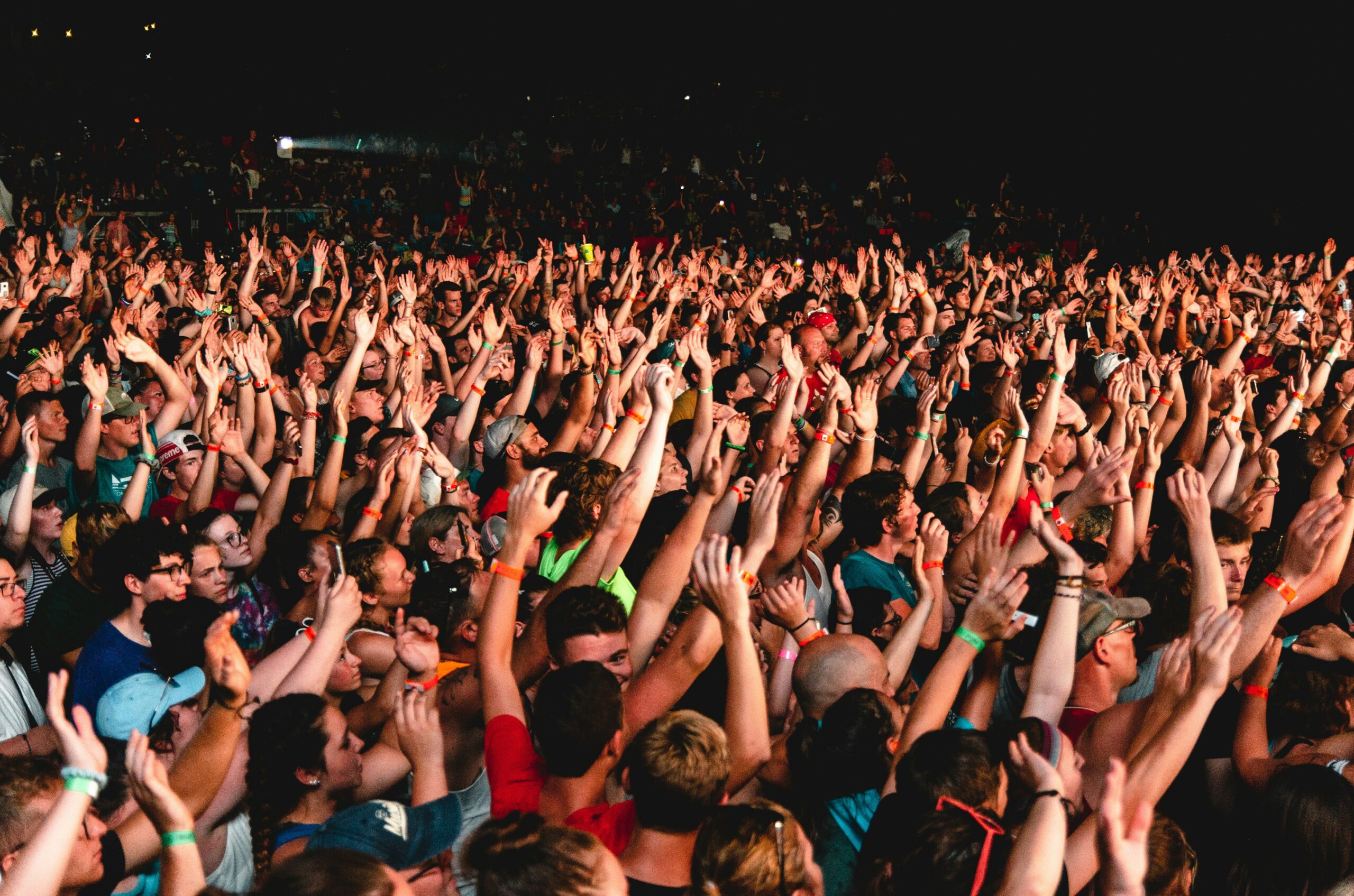 Crowd of concertgoers with raised hands at night, cheering and enjoying a live performance.