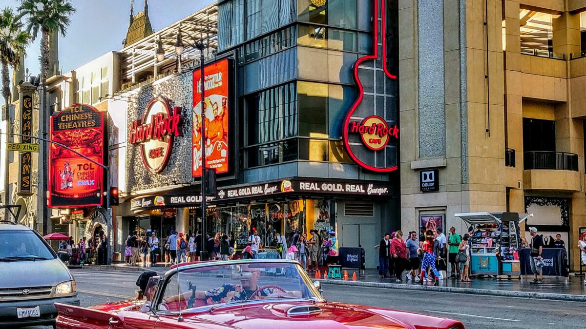 Red vintage convertible cruising down a sunny Hollywood street with the Hard Rock Cafe guitar sign and Dolby Theatre in the background.