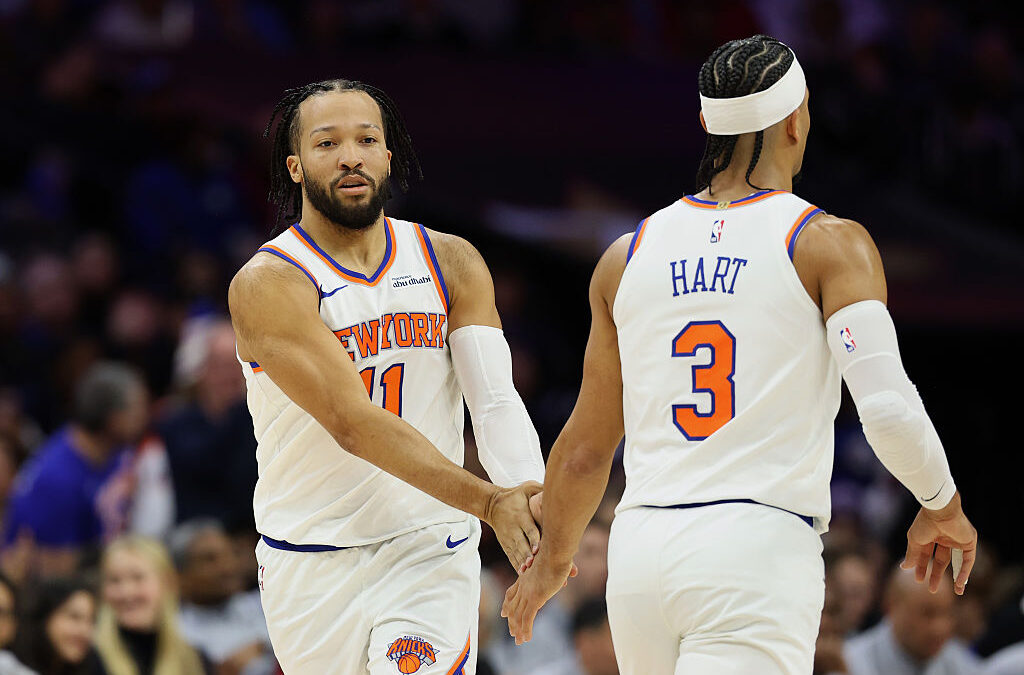 Two basketball players in white New York Knicks uniforms high-five on the court during a game.