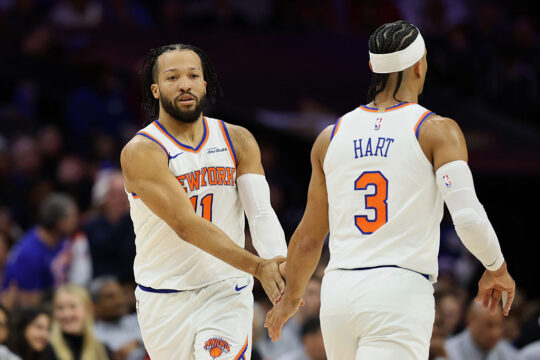 Two basketball players in white New York Knicks uniforms high-five on the court during a game.