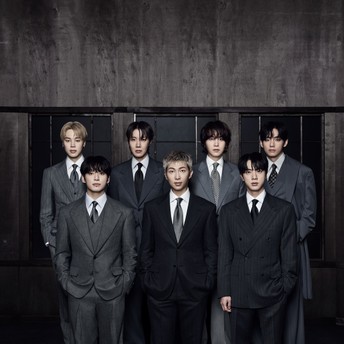 Seven men in dark suits posing together for a formal group portrait against a dark background.
