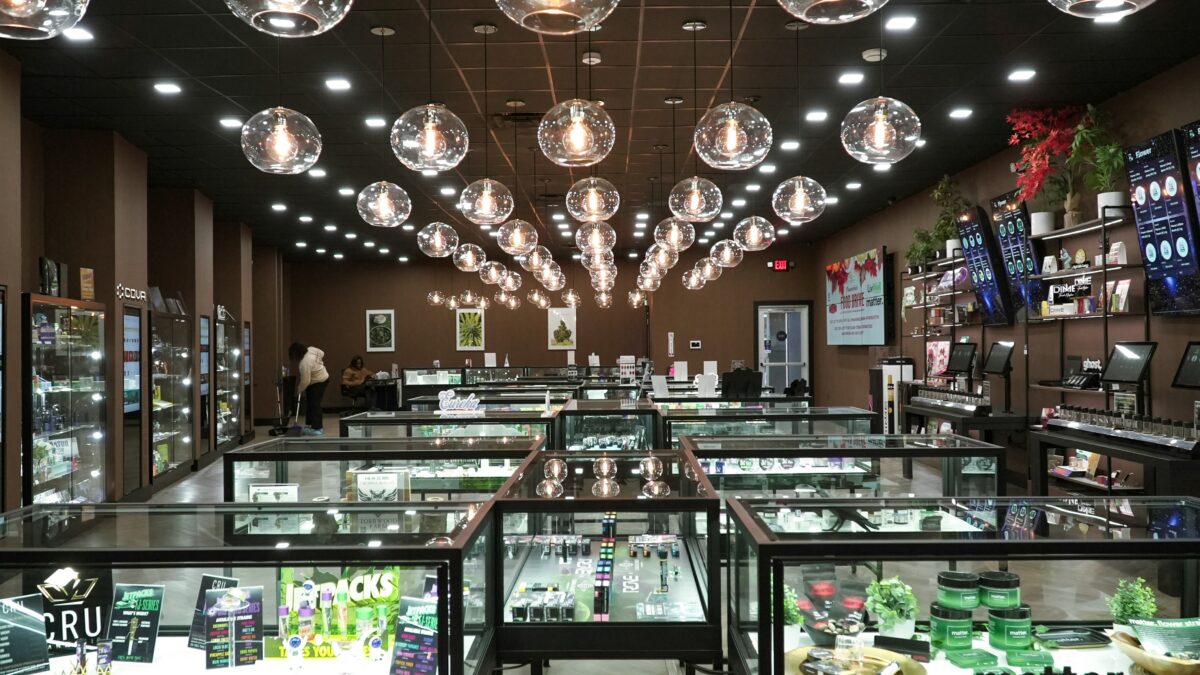 Interior of a cannabis shop with glass display cases, wall menus, and round glass pendant lights overhead