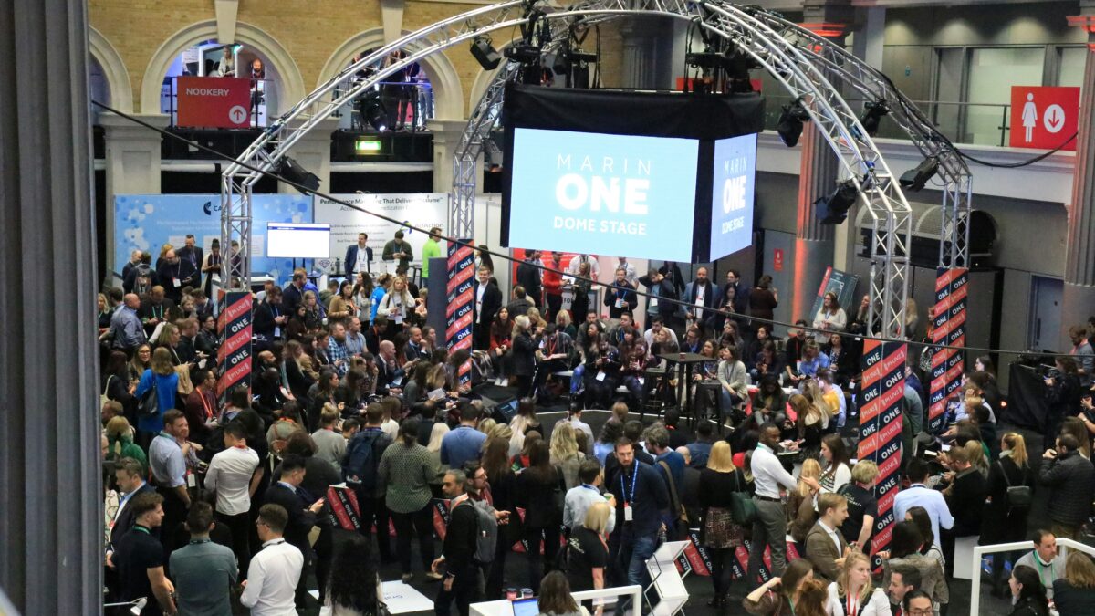 Busy conference hall with a large suspended stage screen reading 'Marin One Dome Stage' surrounded by truss arches and a crowd of attendees.