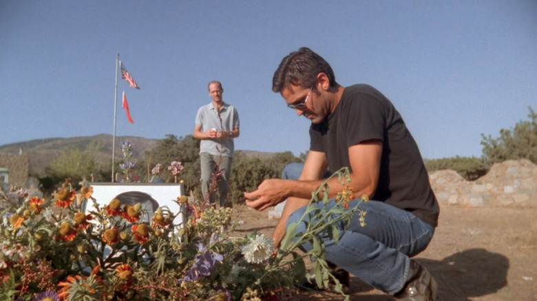 Goerge Clooney as Doug kneeling beside a memorial with Anthony Edwards as Mark in the background in ER