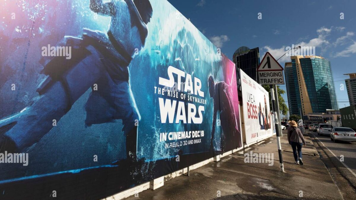Large outdoor wall banner advertising Star Wars: The Rise of Skywalker along a city sidewalk, with a person walking and tall buildings in the background, blue sky visible.