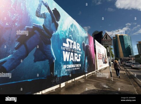 Large outdoor wall banner advertising Star Wars: The Rise of Skywalker along a city sidewalk, with a person walking and tall buildings in the background, blue sky visible.