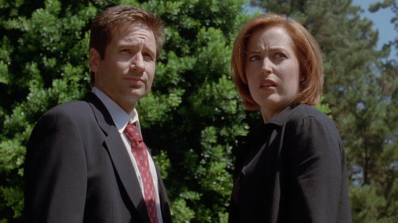 David Duchovny wearing a black suit, white shirt and red tie as Fox Mulder while standing next to Gillian Anderson wearing a black coat as Dana Scully in "The X-Files."