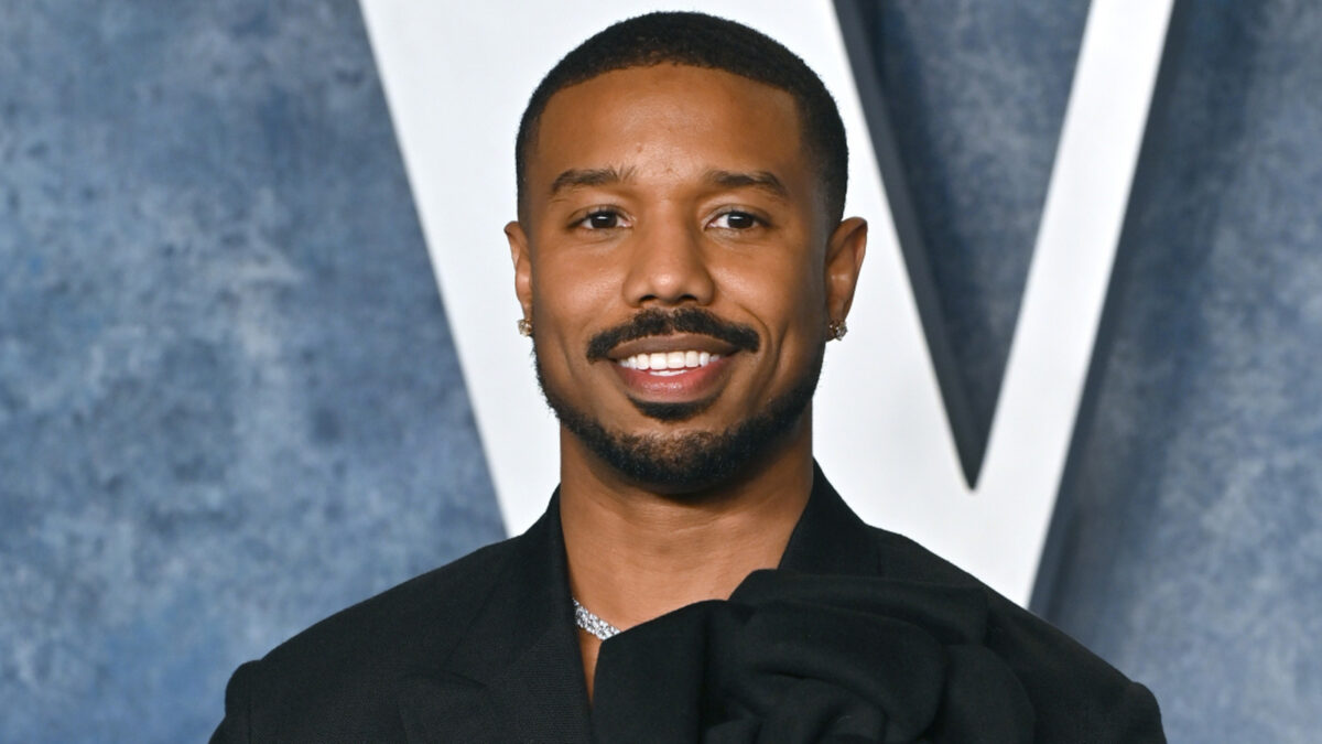 Smiling man with short hair and trimmed beard in a black blazer at a formal event.