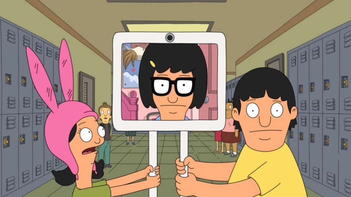 Two students in a school hallway hold a sign showing a cartoon portrait on a screen with glasses and black hair.