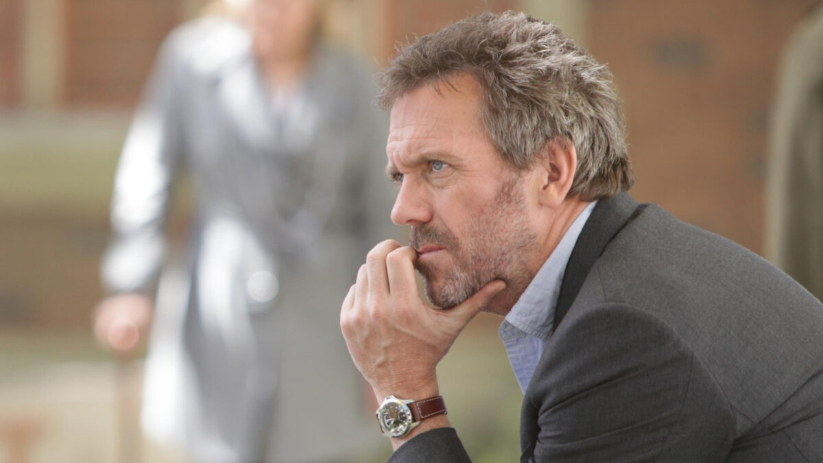 Contemplative man in a blazer outdoors, resting his chin on his hand while looking to the side, wearing a watch.