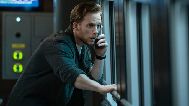 Man in a dark shirt leans on a server cabinet, talking on a handheld phone in a data center.