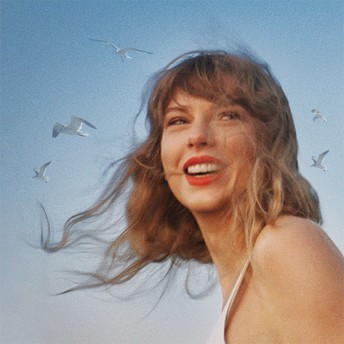 Young woman with windblown hair and a white top smiling against a blue sky with seagulls flying.