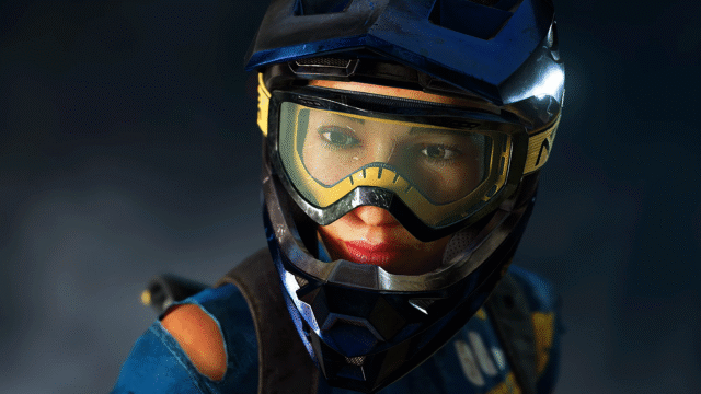 Close-up of a rider wearing a blue motocross helmet and yellow goggles, looking at the camera.