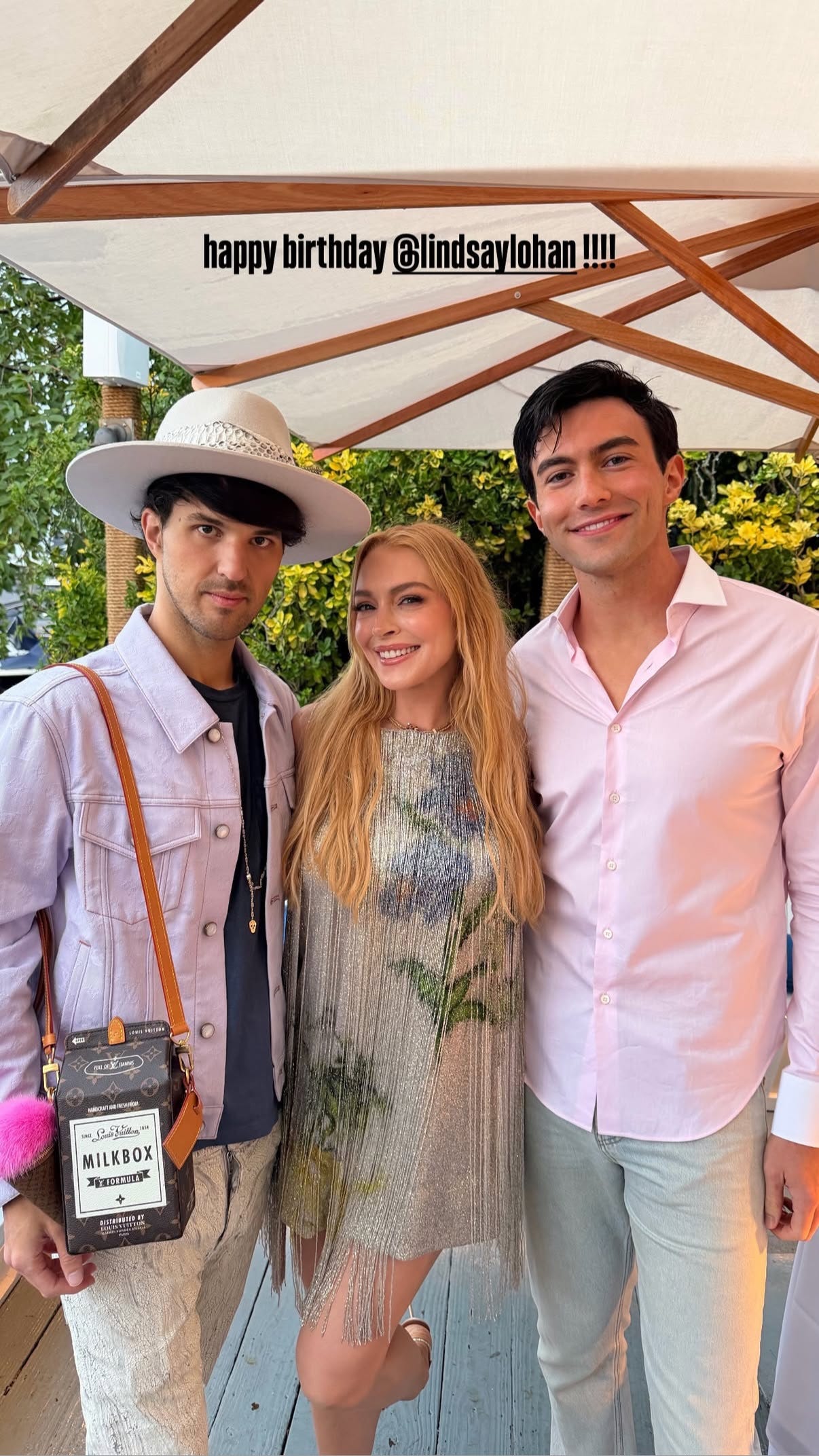 Three people celebrating a birthday outdoors, with festive attire and a decorative backdrop.