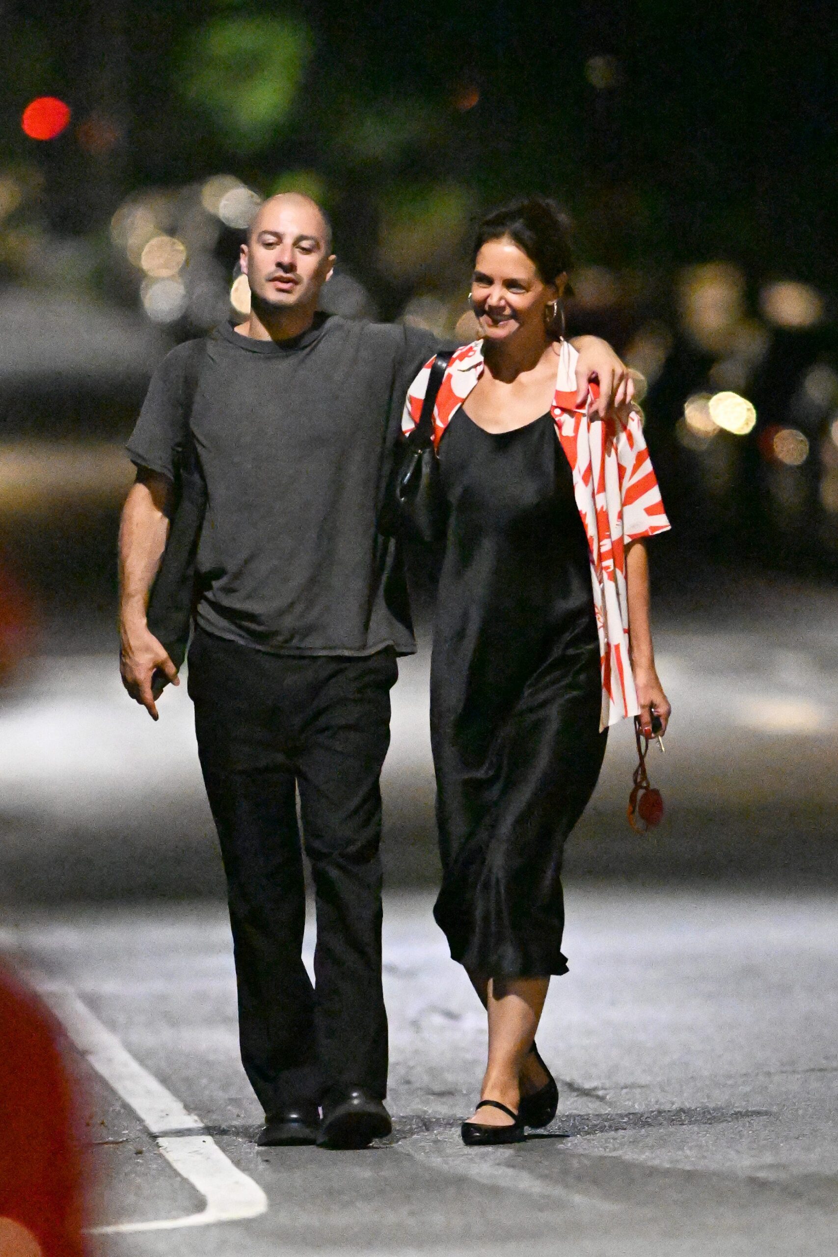 A couple walking closely together at night on a quiet street, smiling and enjoying each other's company.