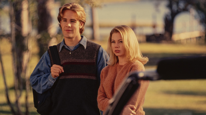 James Van Der Beek as Dawson in a denim shirt and brown vest, standing next to Michelle Williams as Jen in a brown sweater in 'Dawson's Creek.'