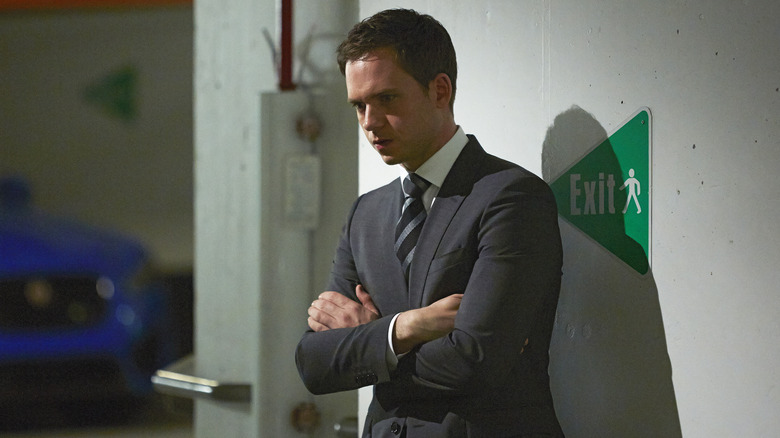 Patrick J. Adams as Mike Ross wearing a grey suit and a stripped tie while standing in a parking lot with his arms crossed in "Suits."