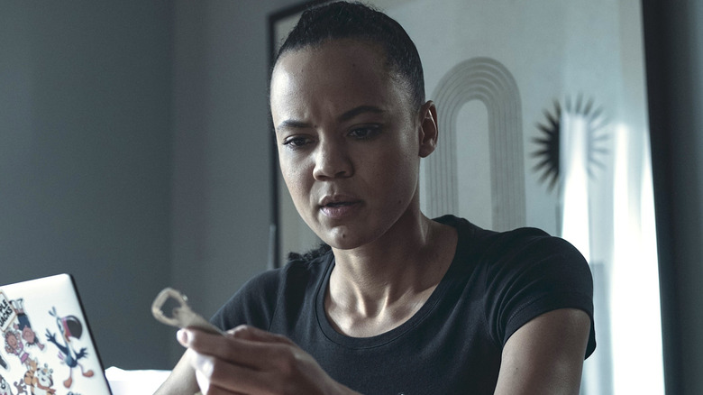 Frances Neagley in a black shirt sitting at a computer and looking at a metal device in Reacher