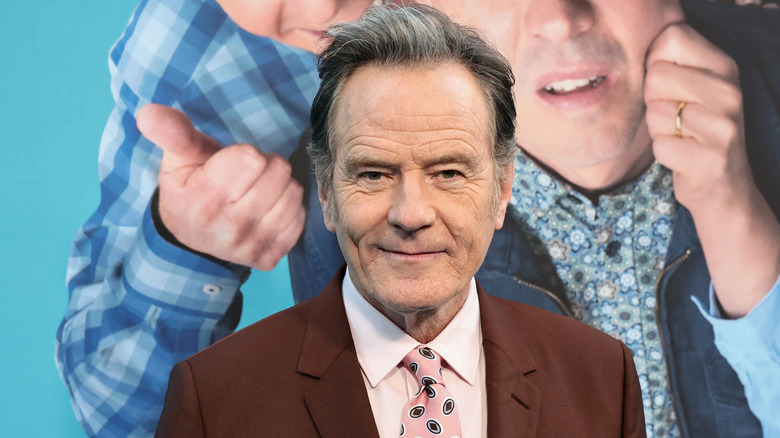 An older man with graying hair looking at the camera. He's wearing a brown suit with a light pink shirt and matching tie.