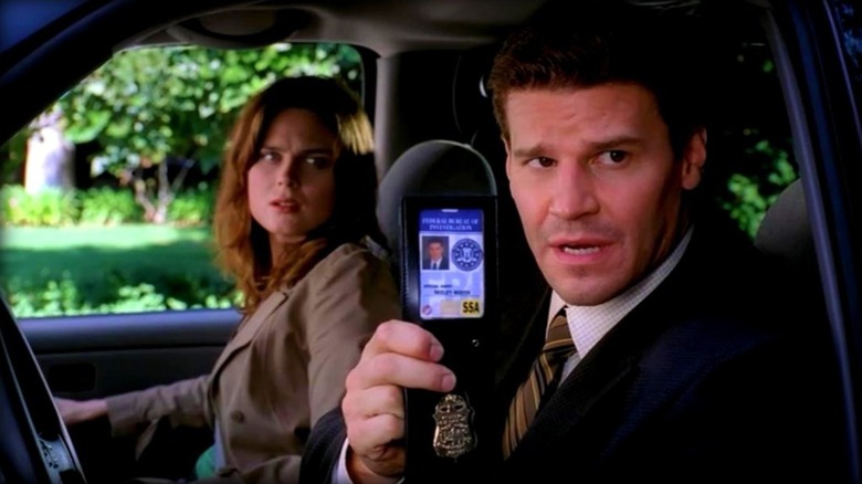 Seeley Booth showing his badge to someone while sitting in a car next to Dr. Temperance "Bones" Brennan