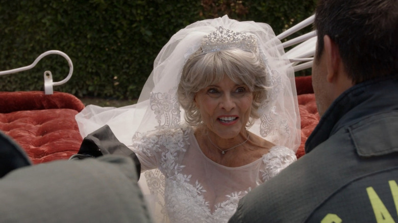 Lois, wearing wedding dress and sitting in carriage in front of firefighters