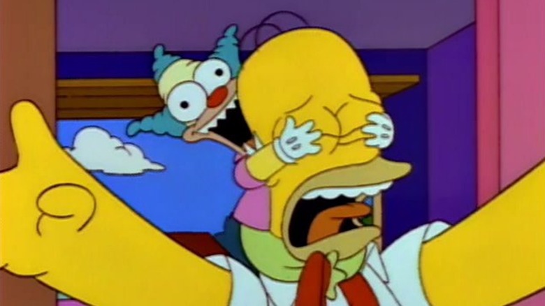 An evil Krusty the Klown doll grabs hold of Homer's head, covering his eyes, on The Simpsons.