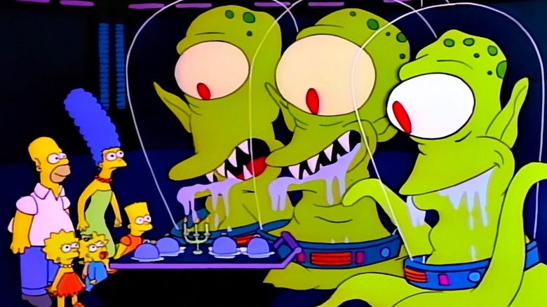 The aliens Kang, Kodos and Serak the Preparer salivate while offering a feast to the Simpsons.