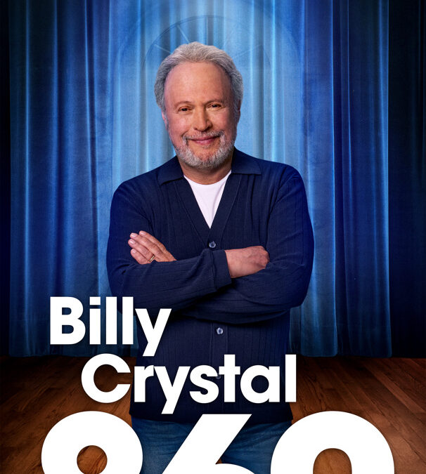 A smiling gray-haired man stands with arms crossed before blue curtains, with large text reading “Billy Crystal 860.”