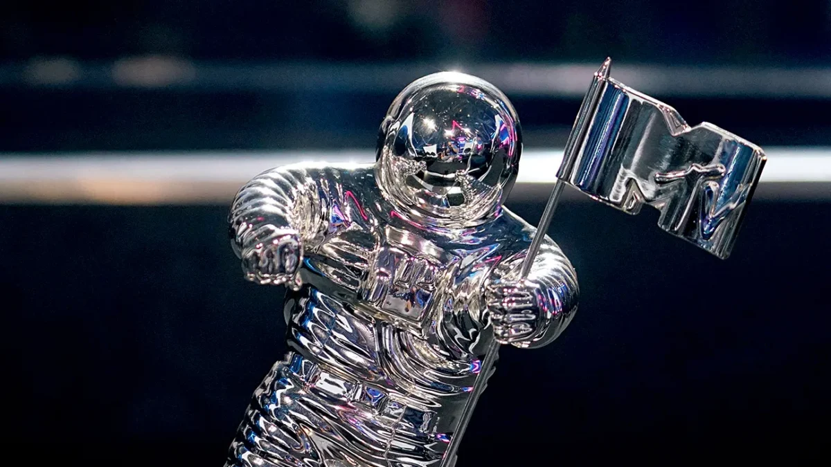 A shiny silver astronaut statuette holds a flag with an MTV logo against a dark blurred background.