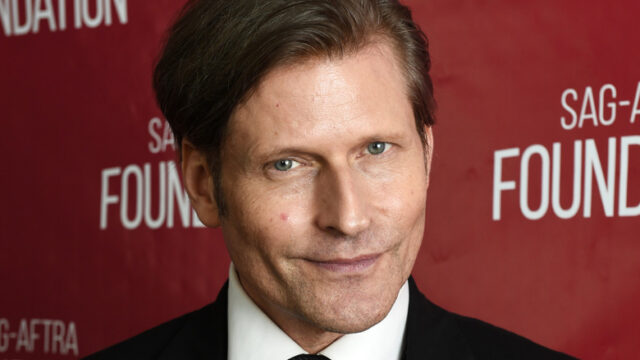 A man in a suit poses in front of a red backdrop with white lettering.