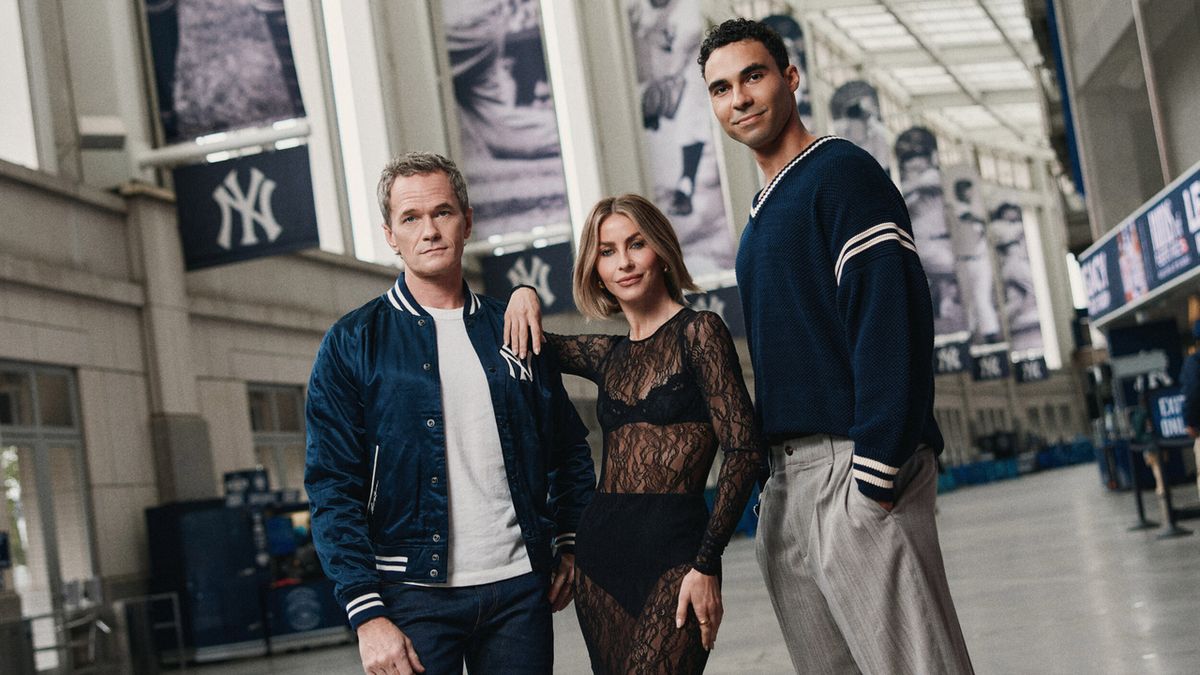 Three people pose in a spacious indoor concourse with large Yankees banners hanging behind them.