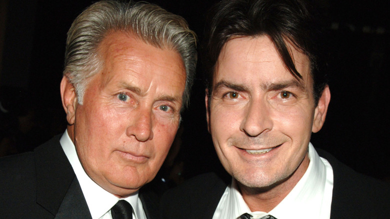 Two men in suits pose closely together against a dark background.