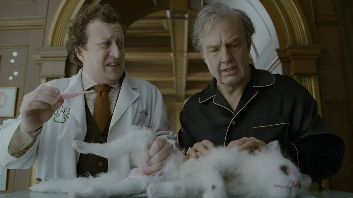 Two men examine a fluffy white cat on a table, one holding a pink toothbrush.