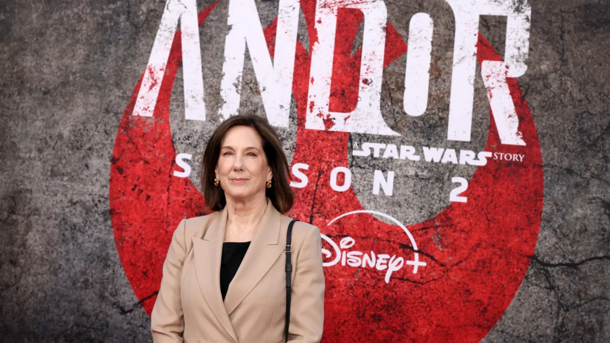 A woman in a tan blazer stands before a large Andor: Star Wars Story Season 2 Disney+ backdrop.