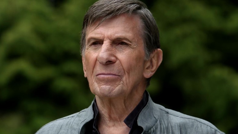 An older man with gray hair and pointed ears looks ahead against a blurred green background.